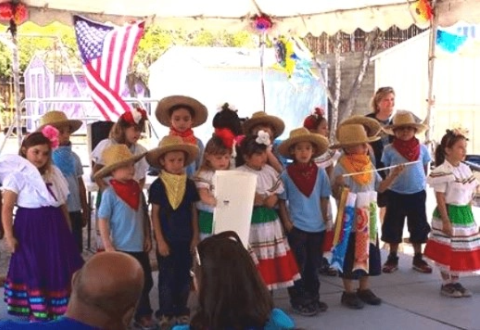 A group of smiling children performing in their school colors. The background shows classroom activities and school facilities.